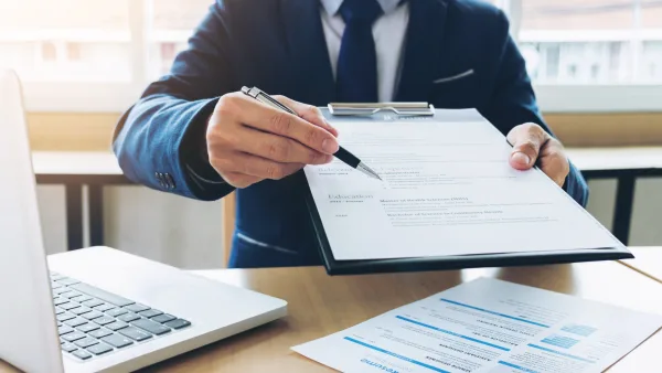 Person behind a desk handing over a clipboard with papers and pen
