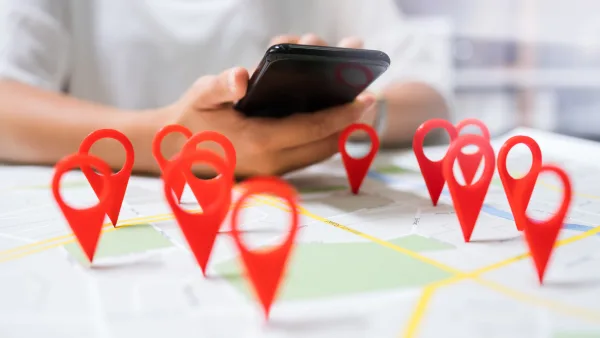 An person looking at their phone near a map with pins marking locations