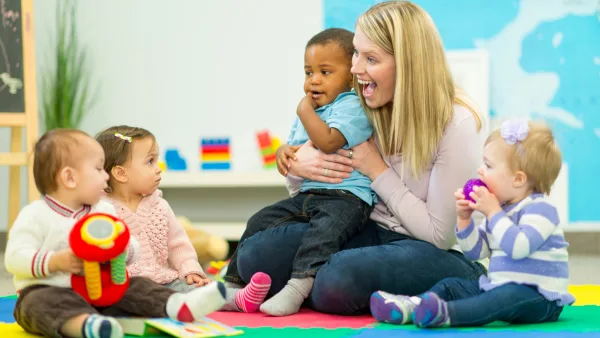 An adult teacher holding a child and smiling at three other children sitting around her